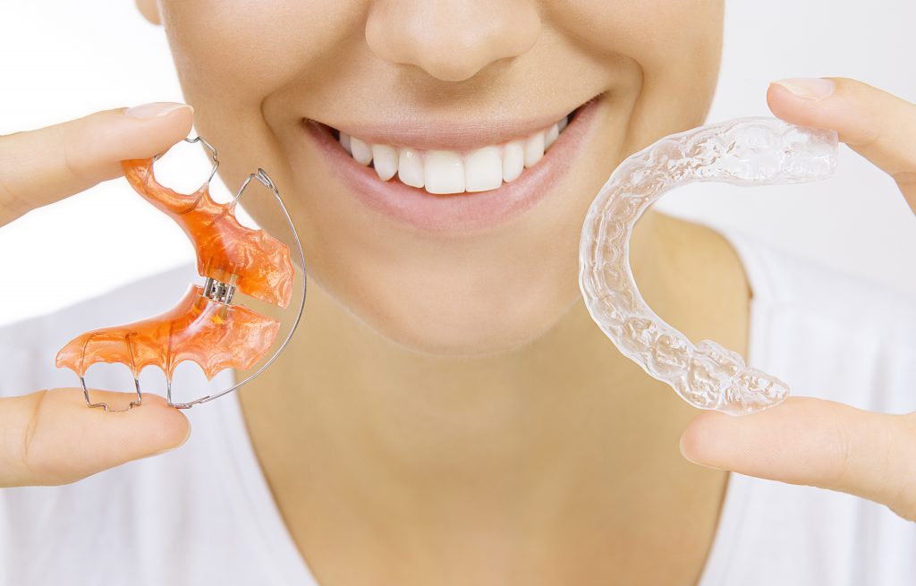 Smiling girl holding retainer for teeth (dental braces) and individual tooth tray