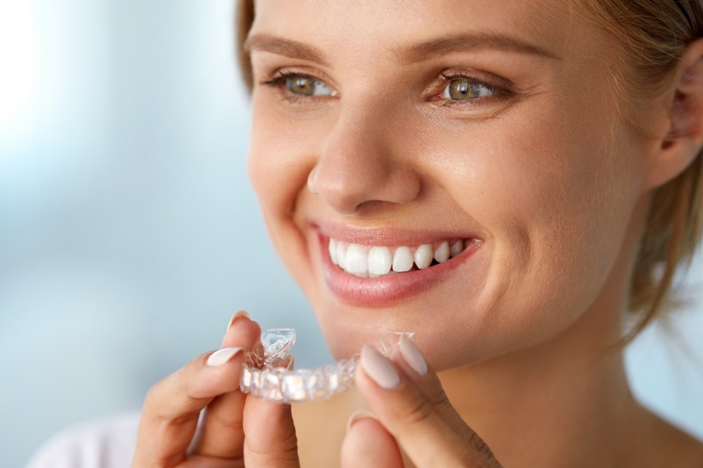 Young adult smiling while holding clear aligner