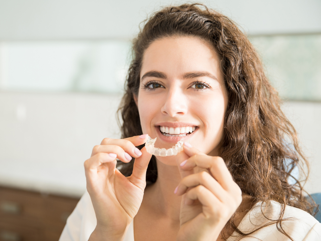 Woman holding a clear orthodontic retainer, showing how to clean retainers for a fresh, hygienic smile.