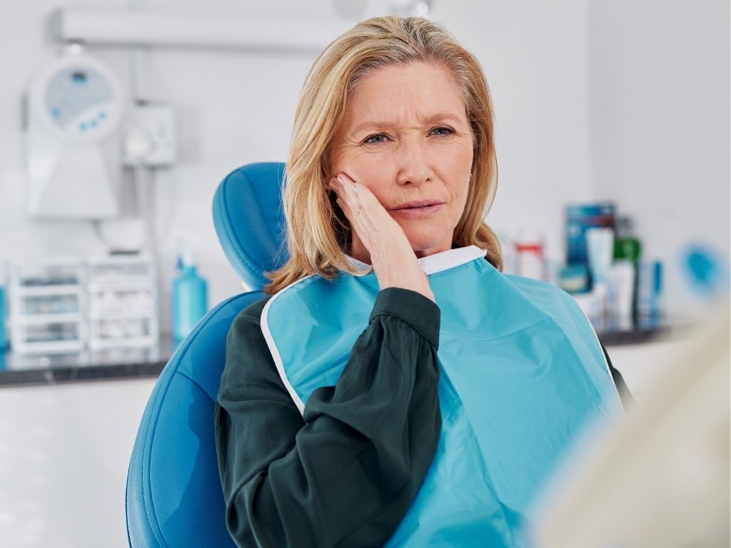 Patient in dental chair holding her jaw in pain, showing symptoms of a bruised tooth during a dental visit.